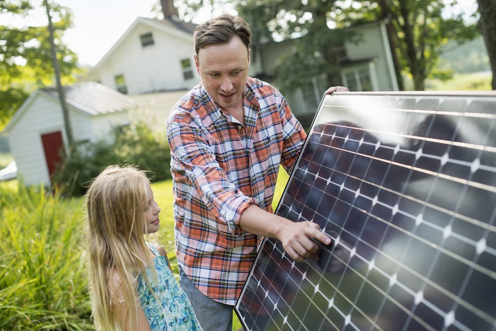 A man and a young girl looking at a solar panel in a garden.