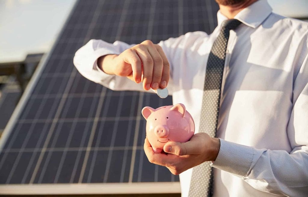 man-in front-of-solar-panels-with-a-piggy-bank